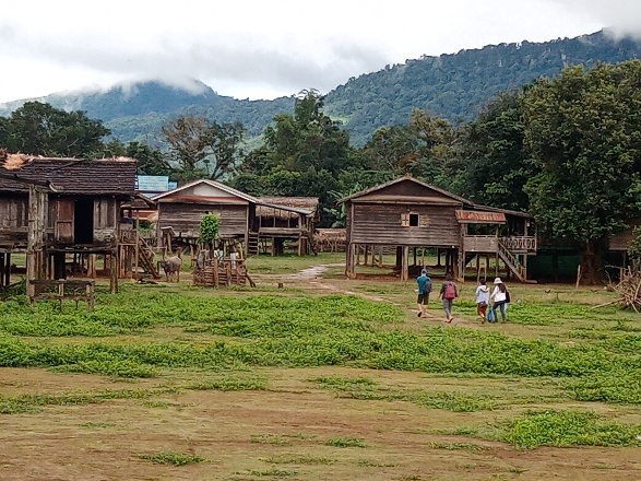 Les maisons en bois sur pilotis du village, devant des collines boisées.