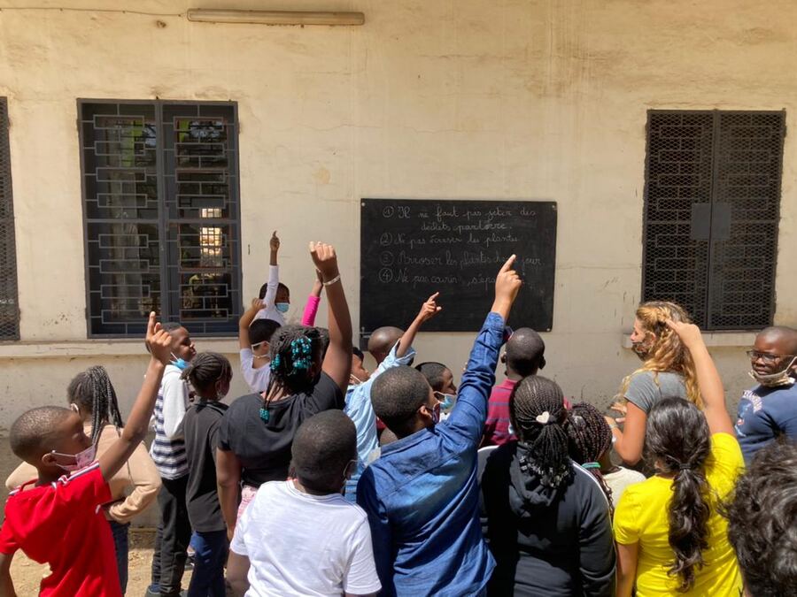 Des enfants lèvent la main pendant un cours en plein air devant le tableau.